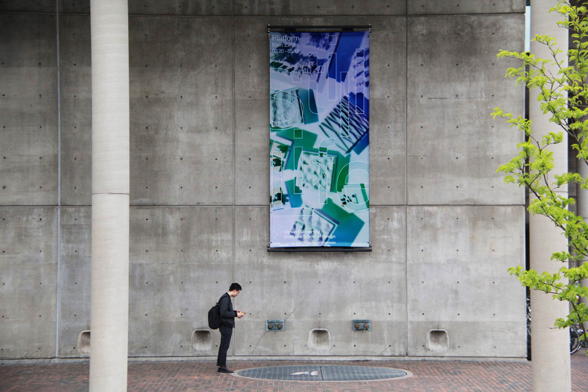 Person standing in front of the Gund Hall featuring the Still Life exhibition banner.