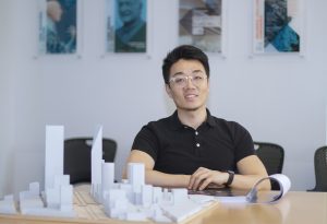 picture of Bing Wang sitting at a table in front of a 3D model of a cityscape