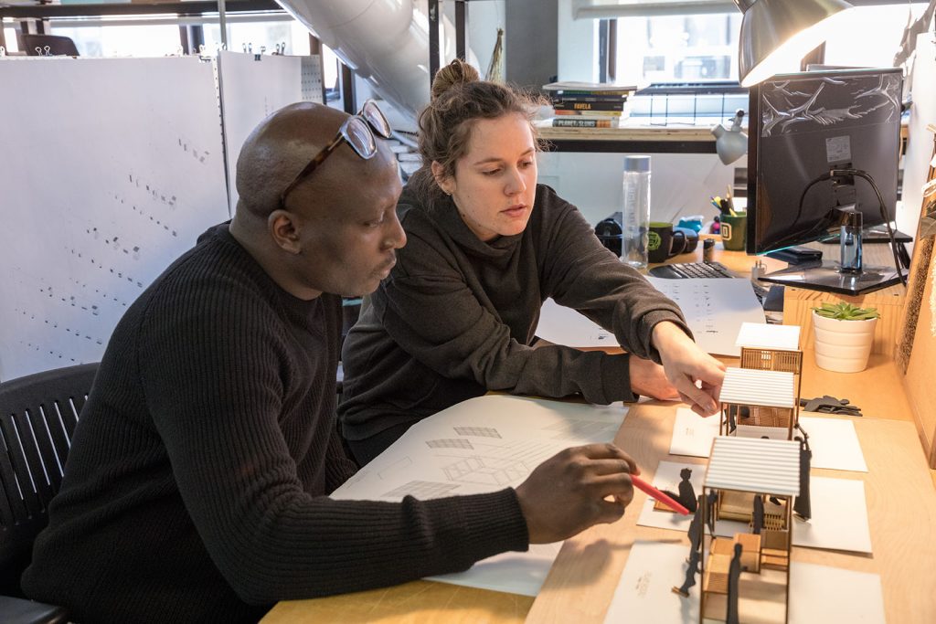 A faculty member and student sit at a desk and look at a project together.