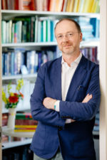 Gareth Doherty in blue blazer standing in front of a shelf of books