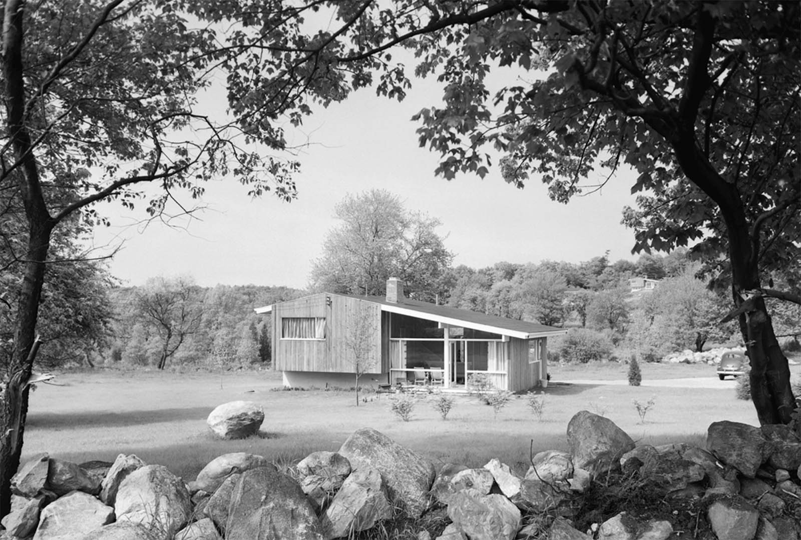 black and white image of a house framed by a stone wall and trees