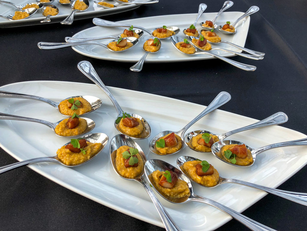 Spoons containing vibrant amuse-bouches laid out on a plate