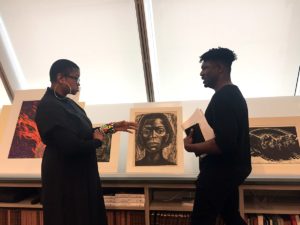 Aisha Densmore and Kay Anthony Jones talking with drawings displayed in a reading room