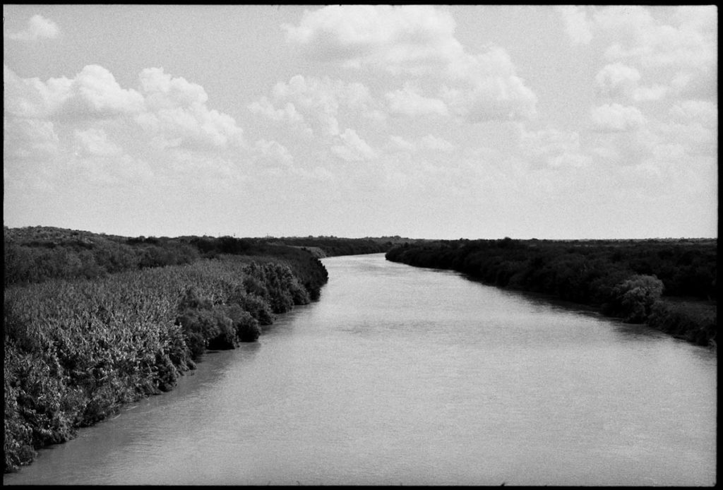 Image by Zoe Leonard from Al Rio/To the River, 2016-2021. A black-and-white photograph shows a wide river along the U.S-Mexico border.