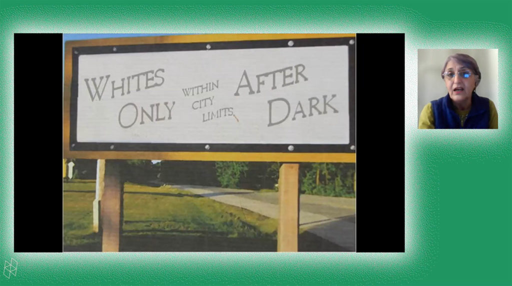 Screenshot from a virtual event. Faranak Miraftab appears in a small square on the right and wears a green shirt and blue vest. A larger rectangle shows her PowerPoint presentation, which contains a photograph of a sign that says "Whites Only Within City Limits After Dark." Faranak and the PowerPoint are surrounded by a green background.