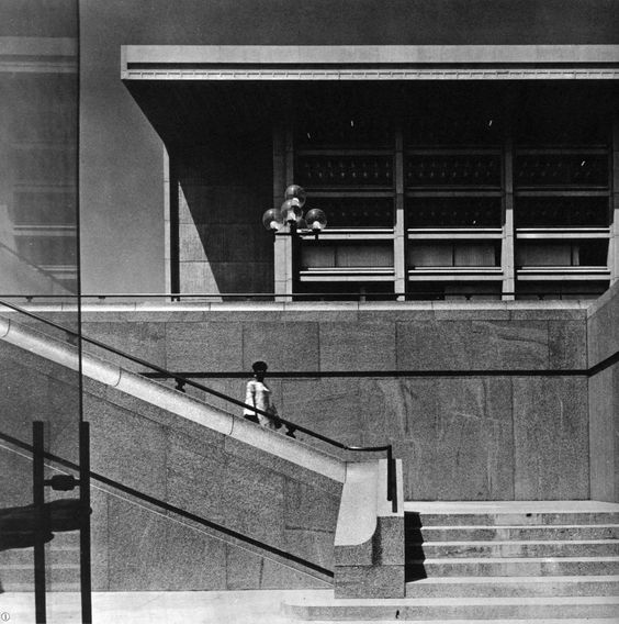 Front steps of L'Enfant Plaza, a brutalist building in black and white, with a woman standing on the front steps.