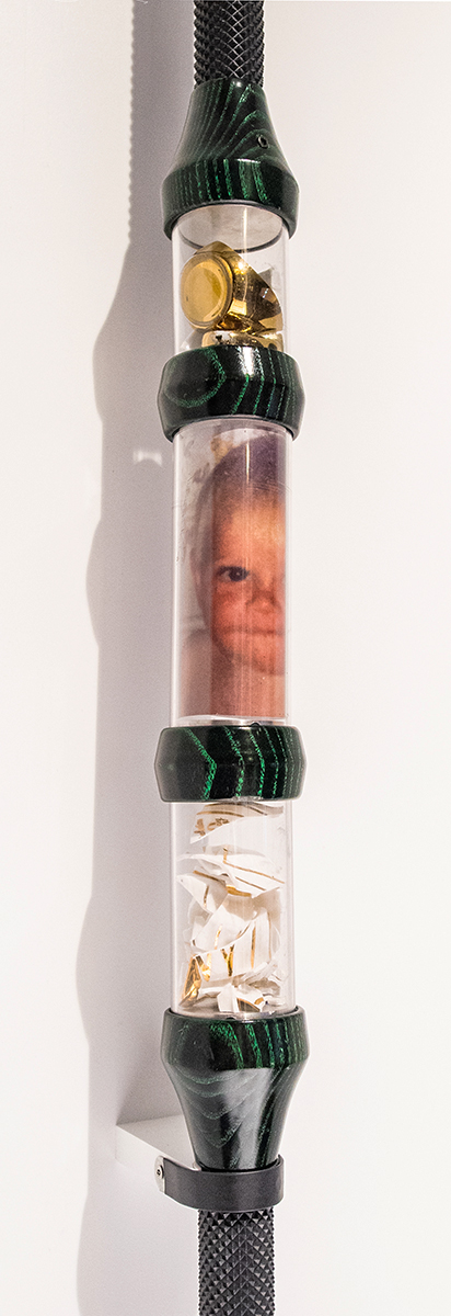 Plexiglass tubing section of the Alien Staff showing three compartments with broken porcelain pieces in the top and bottom, and a photograph of a baby’s face in the middle.