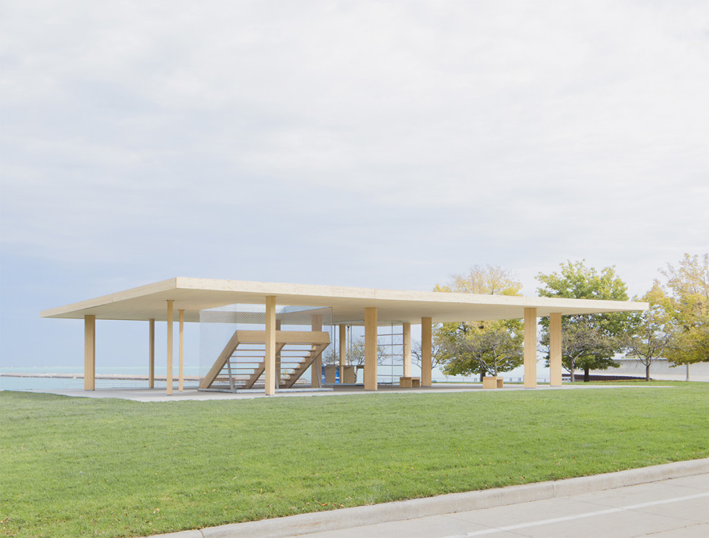 Photograph of grassy field with light wood pavilion featuring a central stair with expansive views of Lake Michigan.