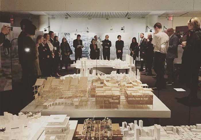 A group of students gather around a city model during final reviews.