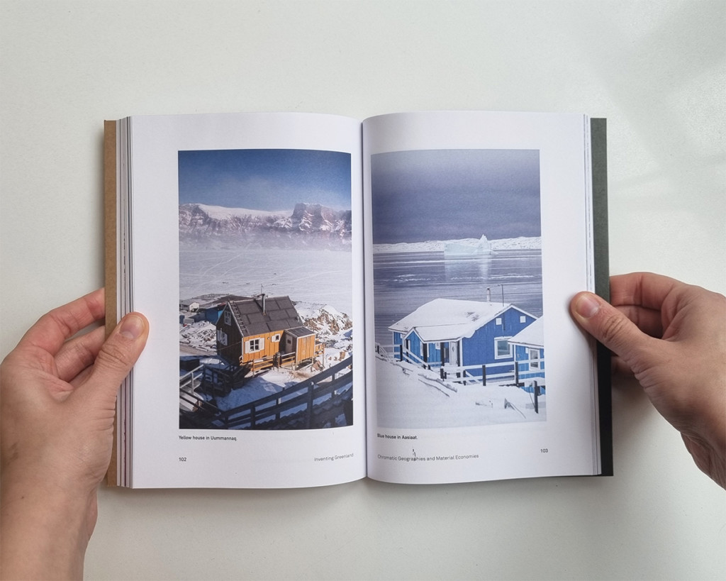 Two hands holding open a book with two photographs of snow-covered homes 