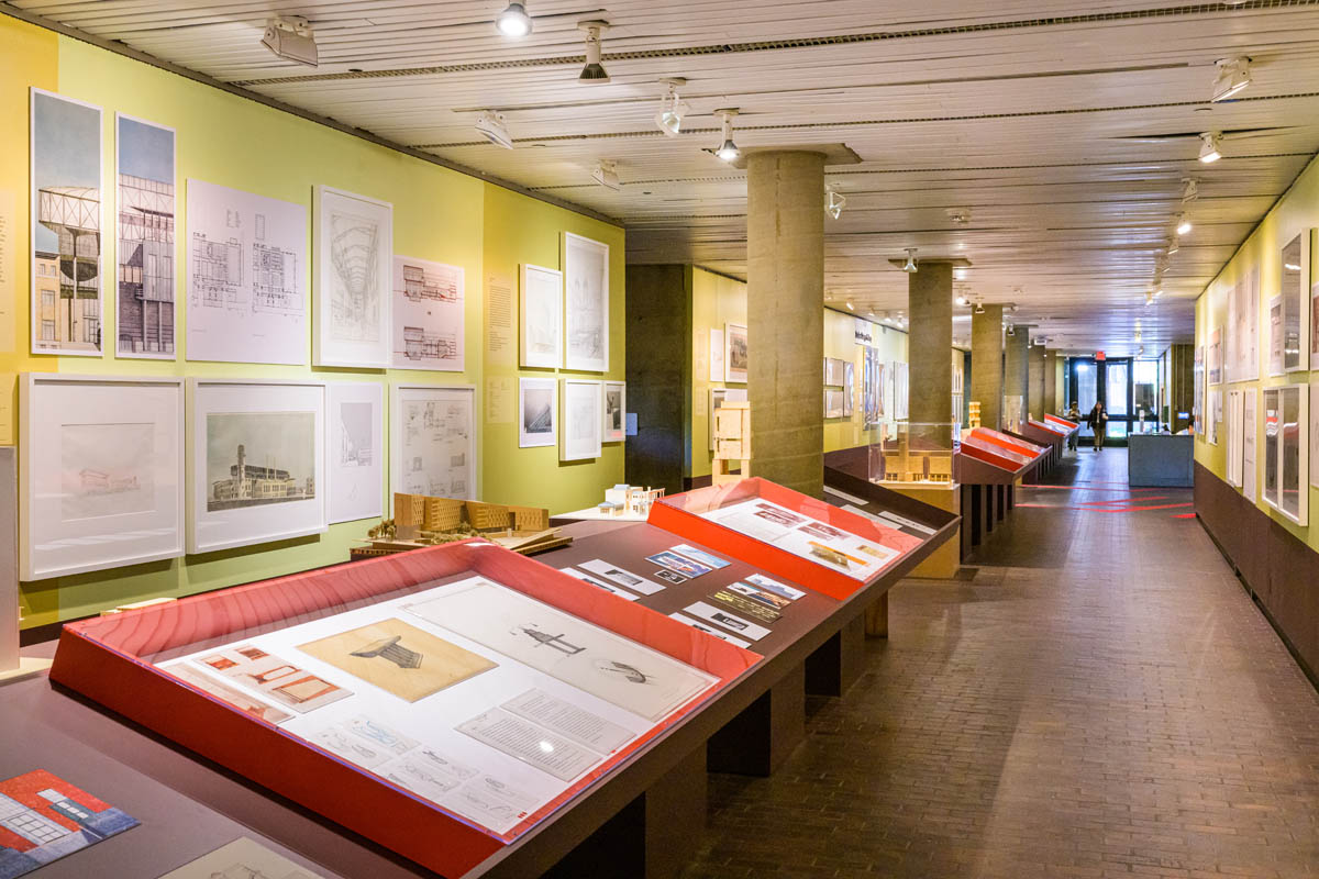 looking down the gallerry cooridor. The walls have framed drawings and full-scale facsimiles. Down the center of the cooridor are long shelves of models, books, text facsimiles and vitrines containing archival artifacts.