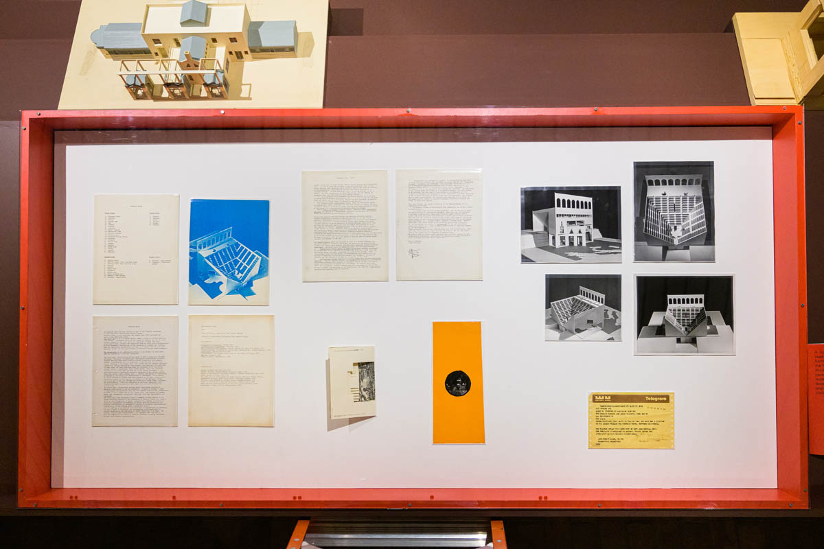 A canted vitrine of archival artifacts (books, memos, photos, and a telegram.)