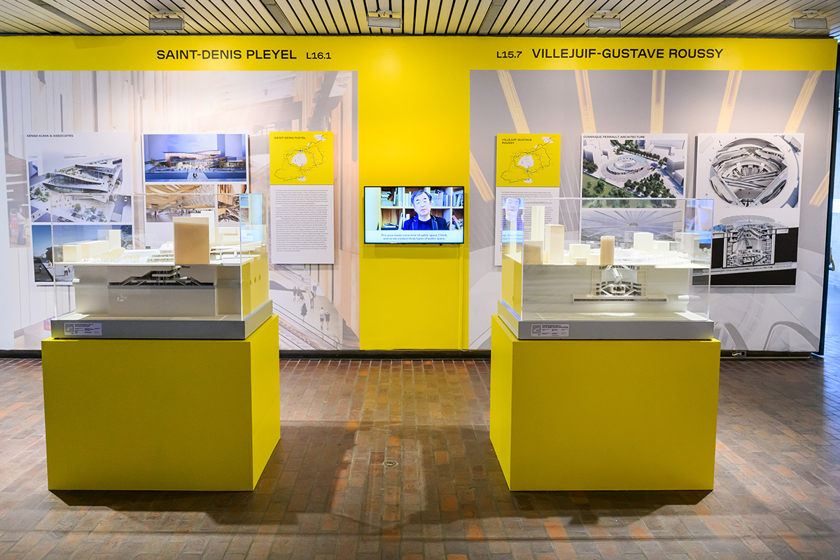 A view of the exhibit with two architectural models on pedestals and images on the wall behind them.