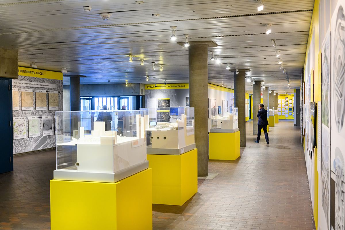 A view of the exhibit showing the lobby of Gund Hall with multiple architectural models on pedestals and images on the walls.
