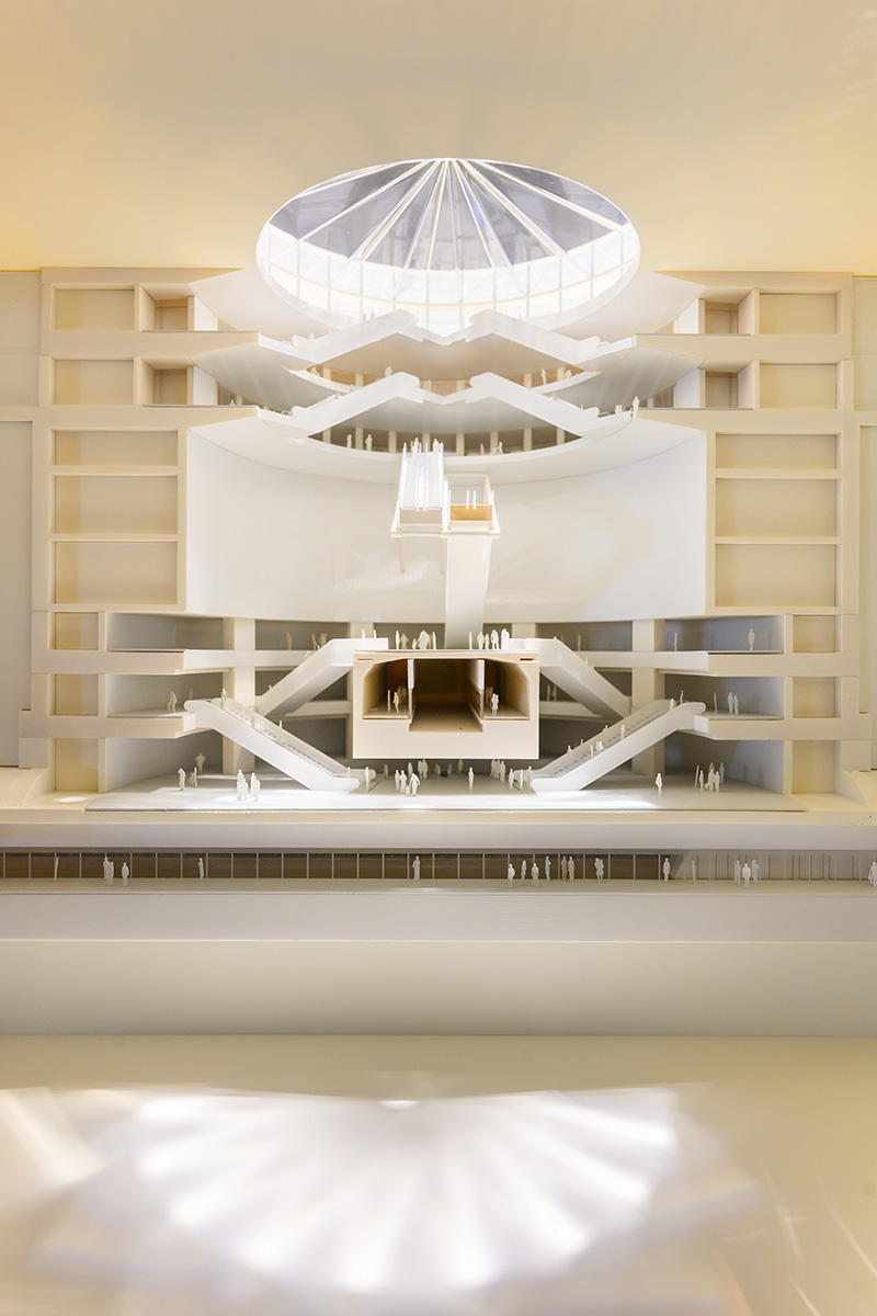 Architectural model of a subway station interior showing multiple stories of stairways and people below a circular skylight.