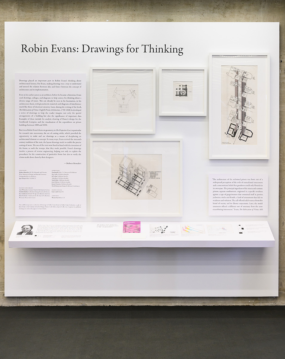 A white wall with framed architectural drawings and text panels above an angled shelf, and the title “Robin Evans: Drawings for Thinking”
