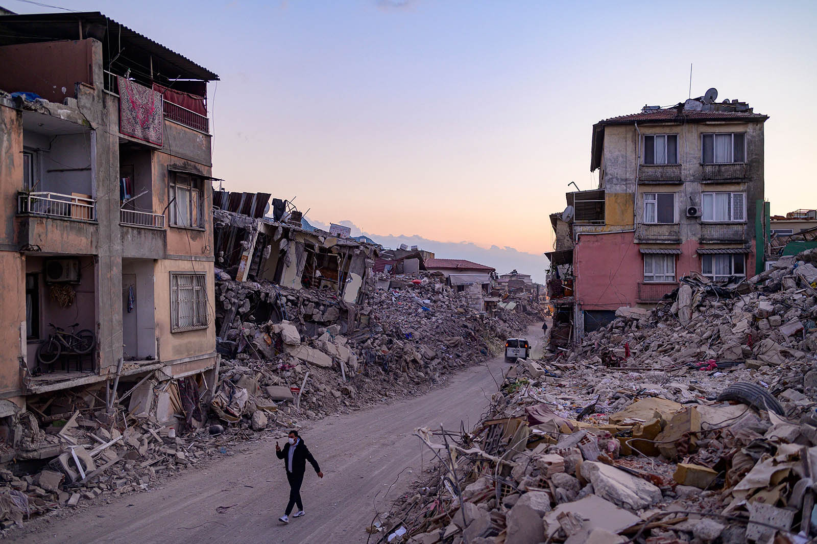 Photo of a man walking in a middle of collapsed buildings with a face mask on.