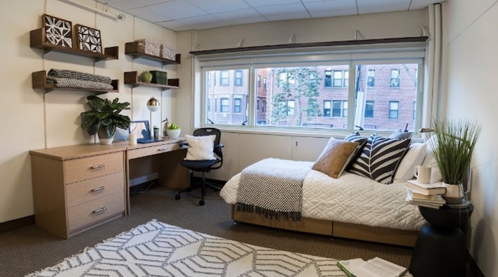 Interior photo of a bed and desk in student housing.