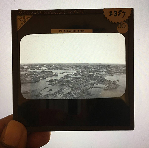 A photograph of pinched fingers holding a slide depicting a black-and-white landscape.